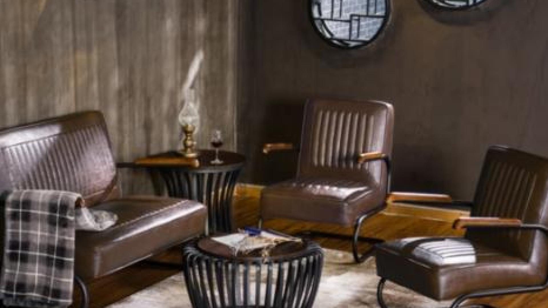 Lounging sofa and chairs surrounded a small, round coffee table. The room is painted in dark colours with a wooden accent wall.