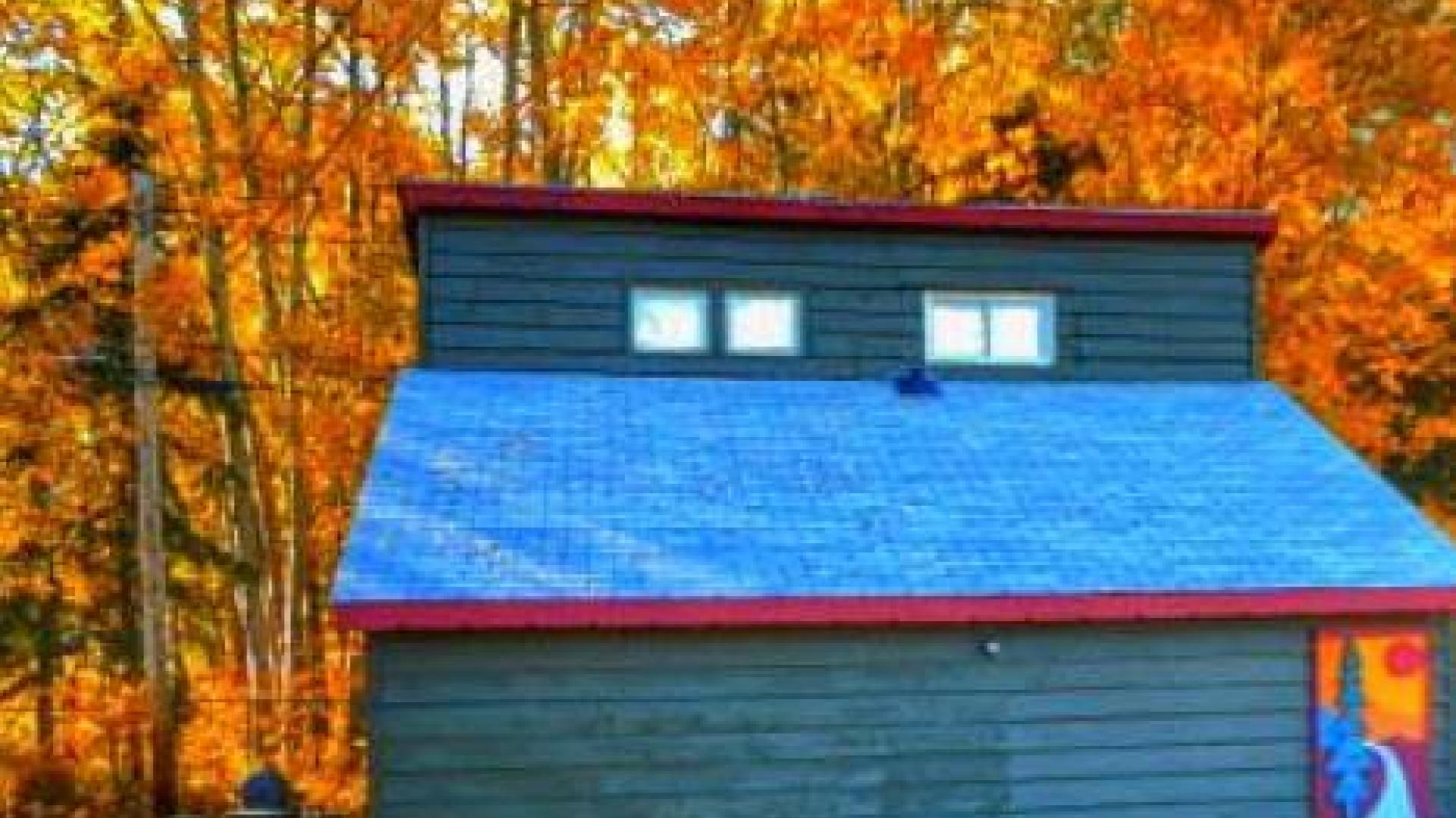 Blue Cabin in the middle of the woods. The trees have orange leaves.