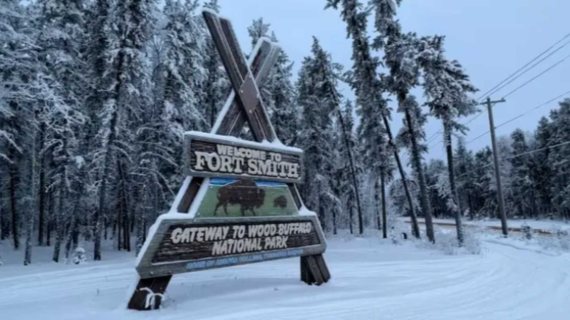 Entrance welcome to fort smith wood sign, surrounded by trees and covered in snow.