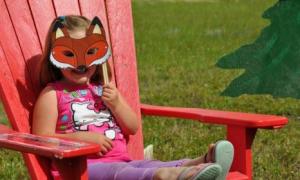 Girl with fox mask sitting on red outdoor lounge chair.