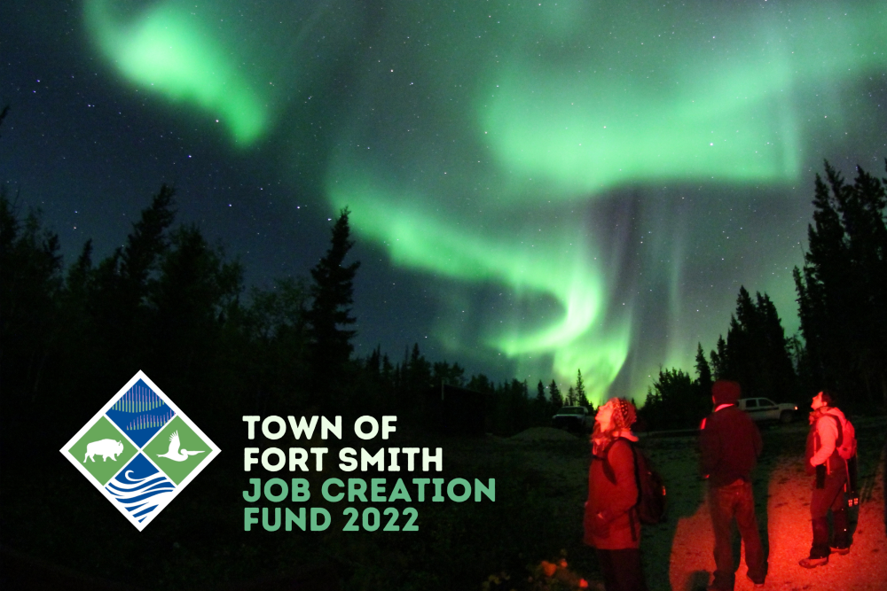 Group of people standing in a red glow looking at the aurora borealis. The words "Town fo Fort Smith Job Creation Fund 2022) are to the bottom left corner.